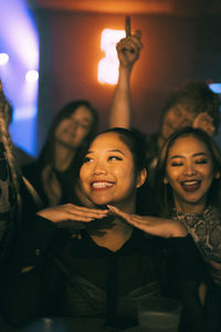 Happy young woman enjoying while dancing with friends in club at night during weekend