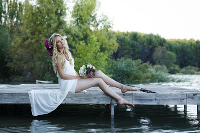 Woman sitting by lake against trees