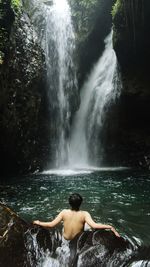 Rear view of shirtless man against waterfall