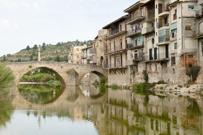 Arch bridge over river by buildings against sky