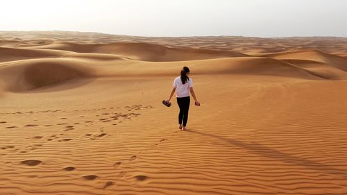 Full length rear view of man walking on sand dune