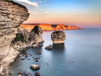 Rock formation in sea against sky during sunset