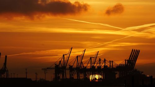 Silhouette of cranes against cloudy sky at sunset