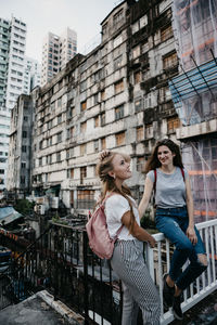 Smiling female friends on bridge against buildings in city