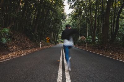 Full length rear view of man running on road in forest