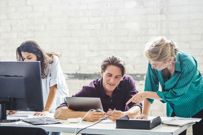 Male computer programmer connecting cable while discussing with female coworker at desk in office