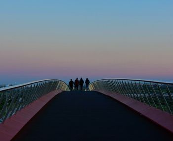 People walking on footbridge against clear sky