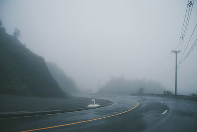 Road by mountain against sky during foggy weather