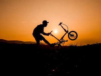 Silhouette man riding bicycle on land against sky during sunset