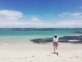 Rear view of woman standing at beach against sky