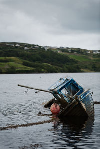 Abandoned boat floating on sea against sky