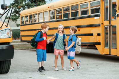 Children boys and girl kids students standing and talking near yellow school bus. 