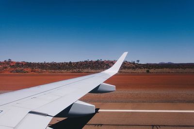 Cropped image of airplane on airport runway against clear blue sky