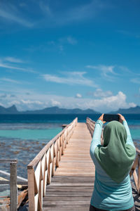 Outdoor portrait of woman in hijab taking photo of the scenery with her smartphone.