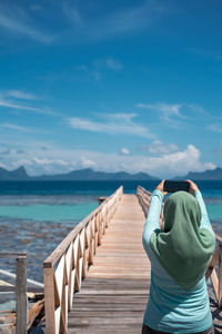 Rear view of woman standing on railing against sea