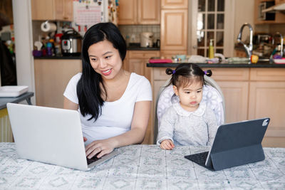 Asian chinese mother with daughter baby working together on laptop, tablet. 