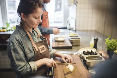 Mature female chef cutting food on board at counter in restaurant kitchen