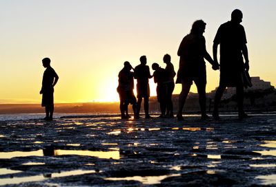 Silhouette people standing on shore at beach against sky during sunset