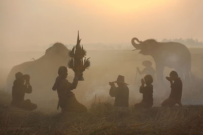 Silhouette people praying on field against sky during sunrise