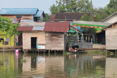 Women washing clothes outside houses by lake against sky