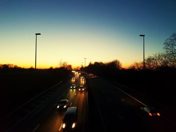 Cars on highway against sky during sunset