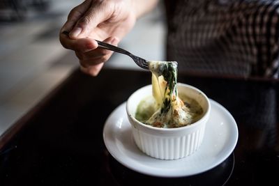 Cropped hand of person holding food in bowl on table