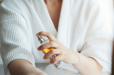 Midsection of woman spraying perfume on hand at home