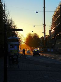 City street by buildings against sky at sunset