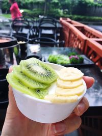 Cropped image of hand holding slices on kiwi and banana in bowl