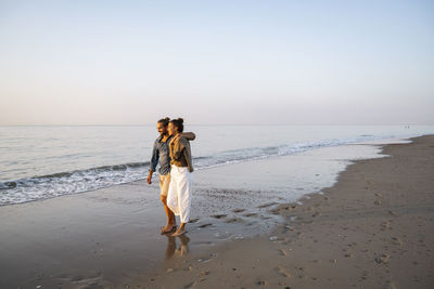 Smiling young couple enjoying sunset at beach against clear sky