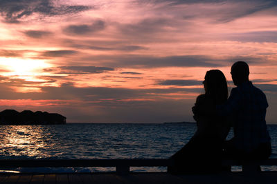 Silhouette couple on sea against sky during sunset