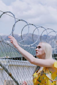 Woman looking at barbed wire against sky