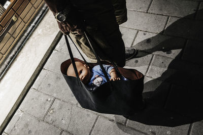 Low section of man holding bag with doll while standing on footpath