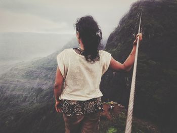 Rear view of man standing on mountain against sky