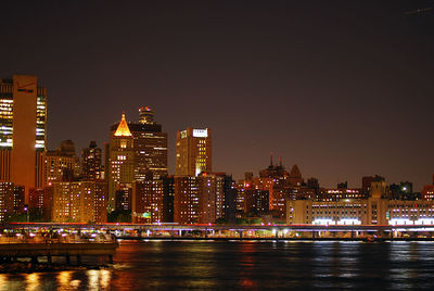 Illuminated buildings by river against sky at night