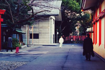 Rear view of people walking on sidewalk by building