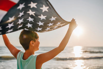 Boy holding american flag at beach during sunset