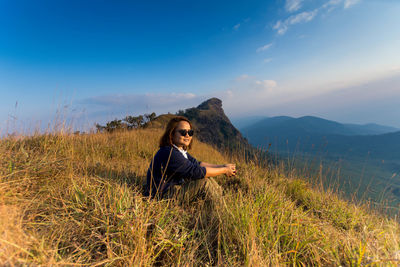 Young woman sitting on grassy mountain against sky