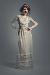 Portrait of beautiful young woman wearing white gown against gray background