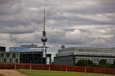 Communications tower in city against cloudy sky