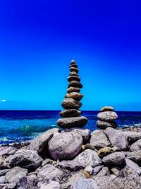 Stack of stones on rock by sea against blue sky