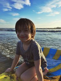 Boy sitting at beach against sky