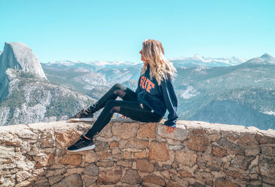 Man sitting on mountain against sky