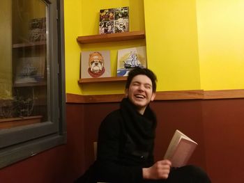Smiling young woman sitting on book at home