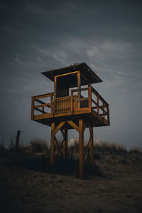 Lifeguard hut on sand against sky at dusk