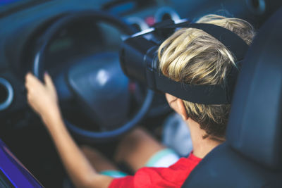 High angle view of boy wearing vr goggles sitting on driver seat of car