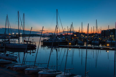 Sailboats moored in harbor at sunset