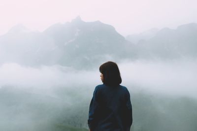 Rear view of woman standing on mountain during foggy weather