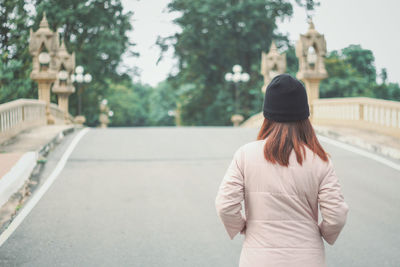 Rear view of woman standing against trees in city