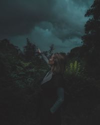 Woman standing by trees in forest against sky at dusk